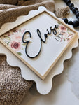 Baby shower gift idea – custom name sign with floral design and 3D lettering, styled with newborn essentials for hospital bag photo.