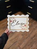 Personalized baby girl name sign displayed in a nursery, with floral details and a scalloped edge frame, perfect for nursery wall decor.